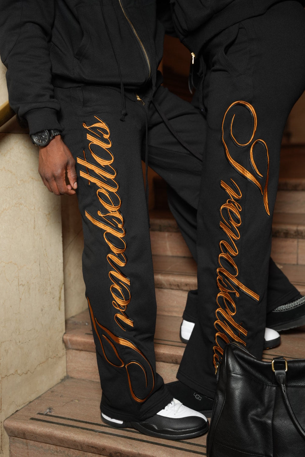 Person wearing a black outfit with 'Trendsettas' branding on a wooden floor.