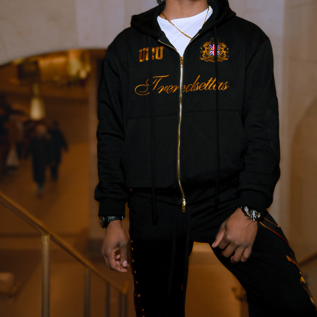 Man wearing a black hoodie with gold text and logos in an indoor setting