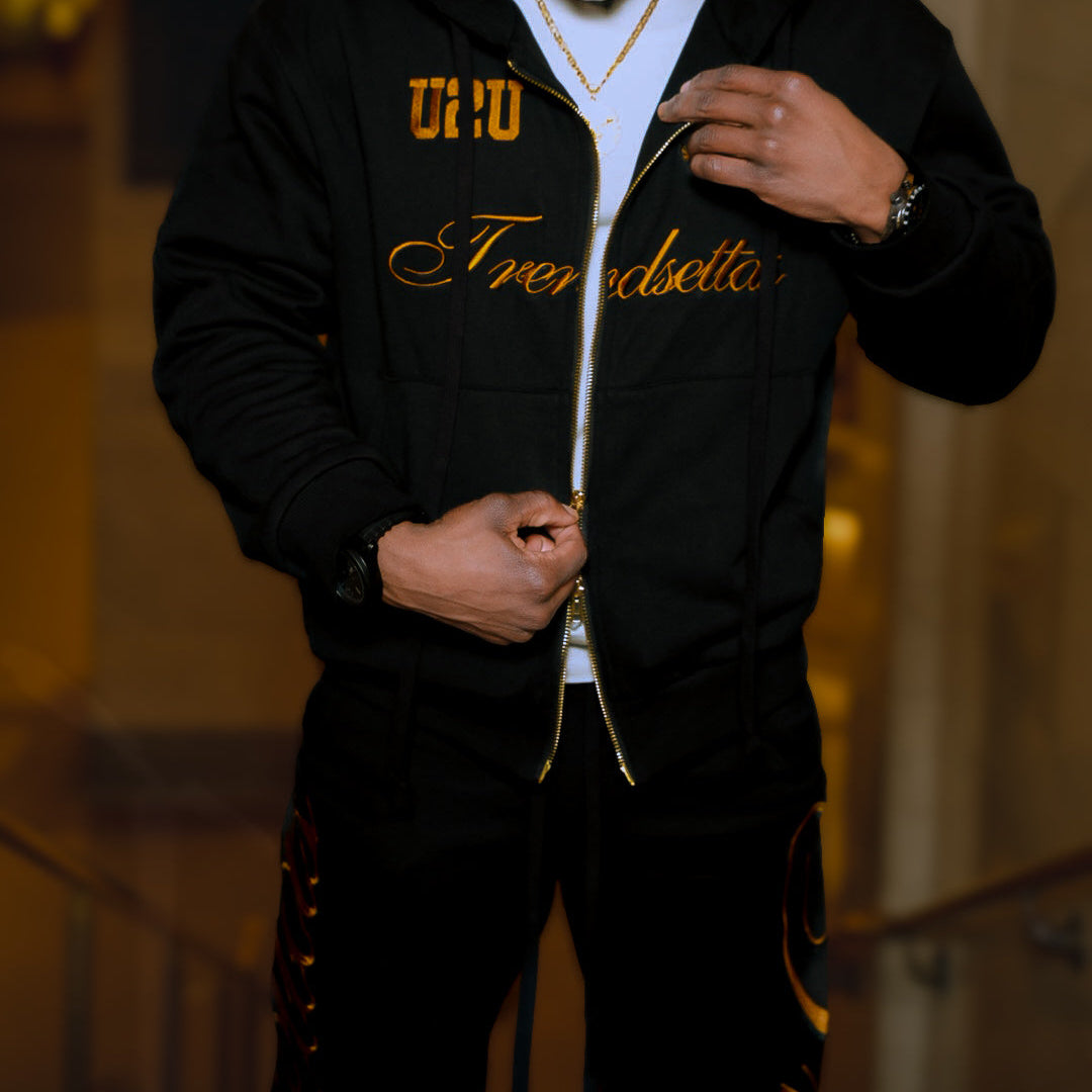 Man wearing a black hoodie with gold text, standing indoors.